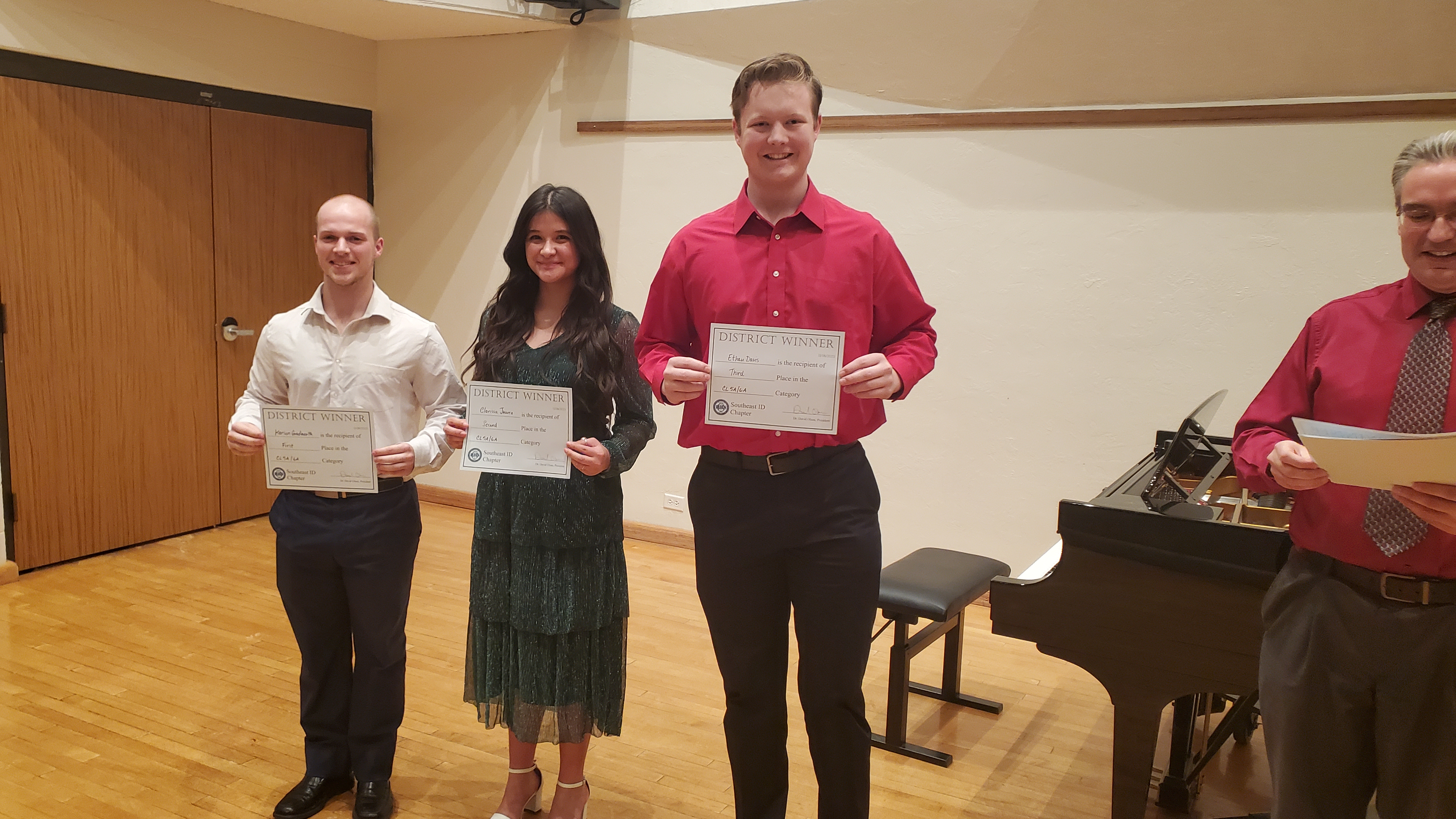 3 winning students pose with certificates in front of a grand piano