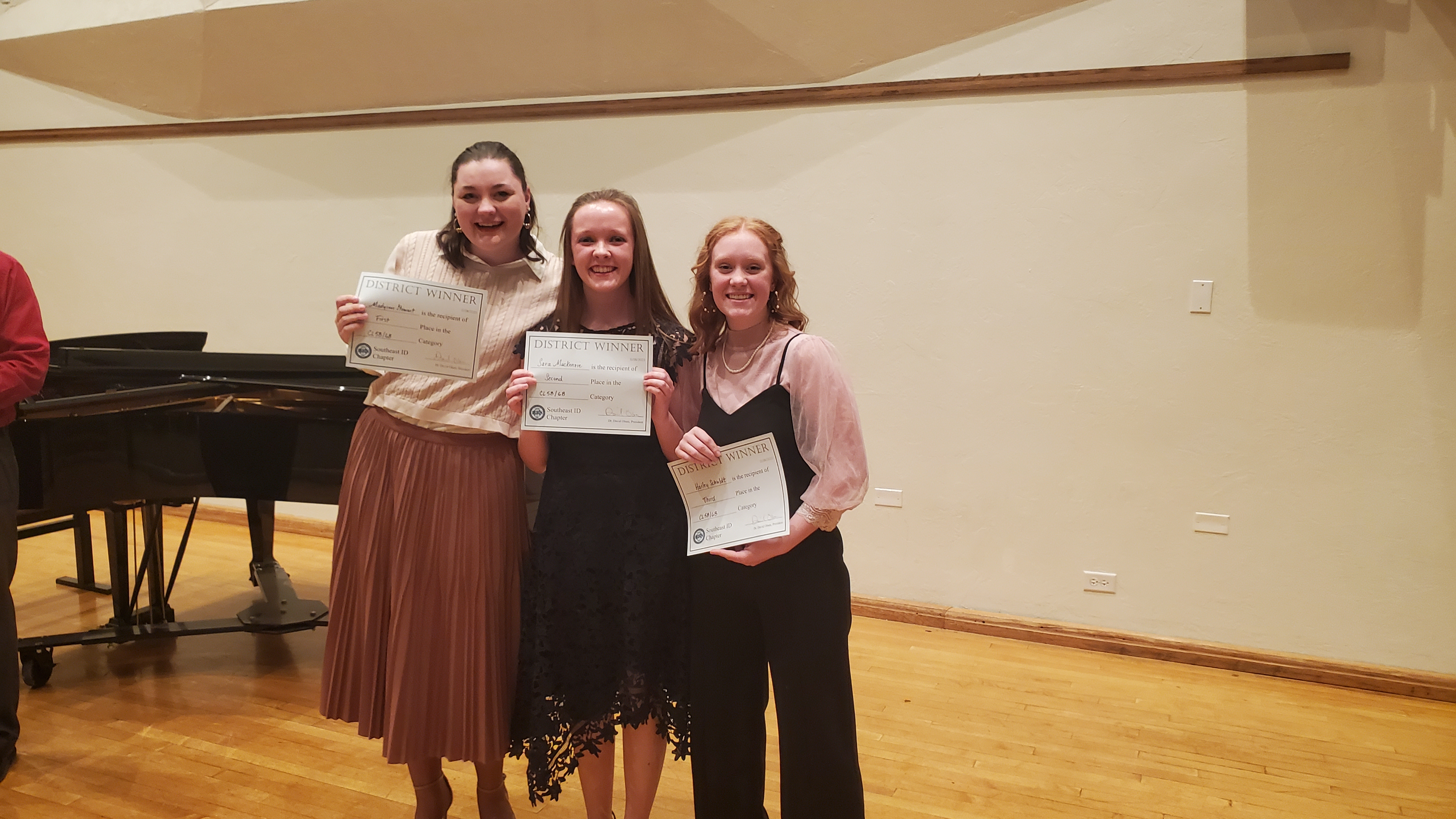 3 winning students pose with certificates in front of a grand piano