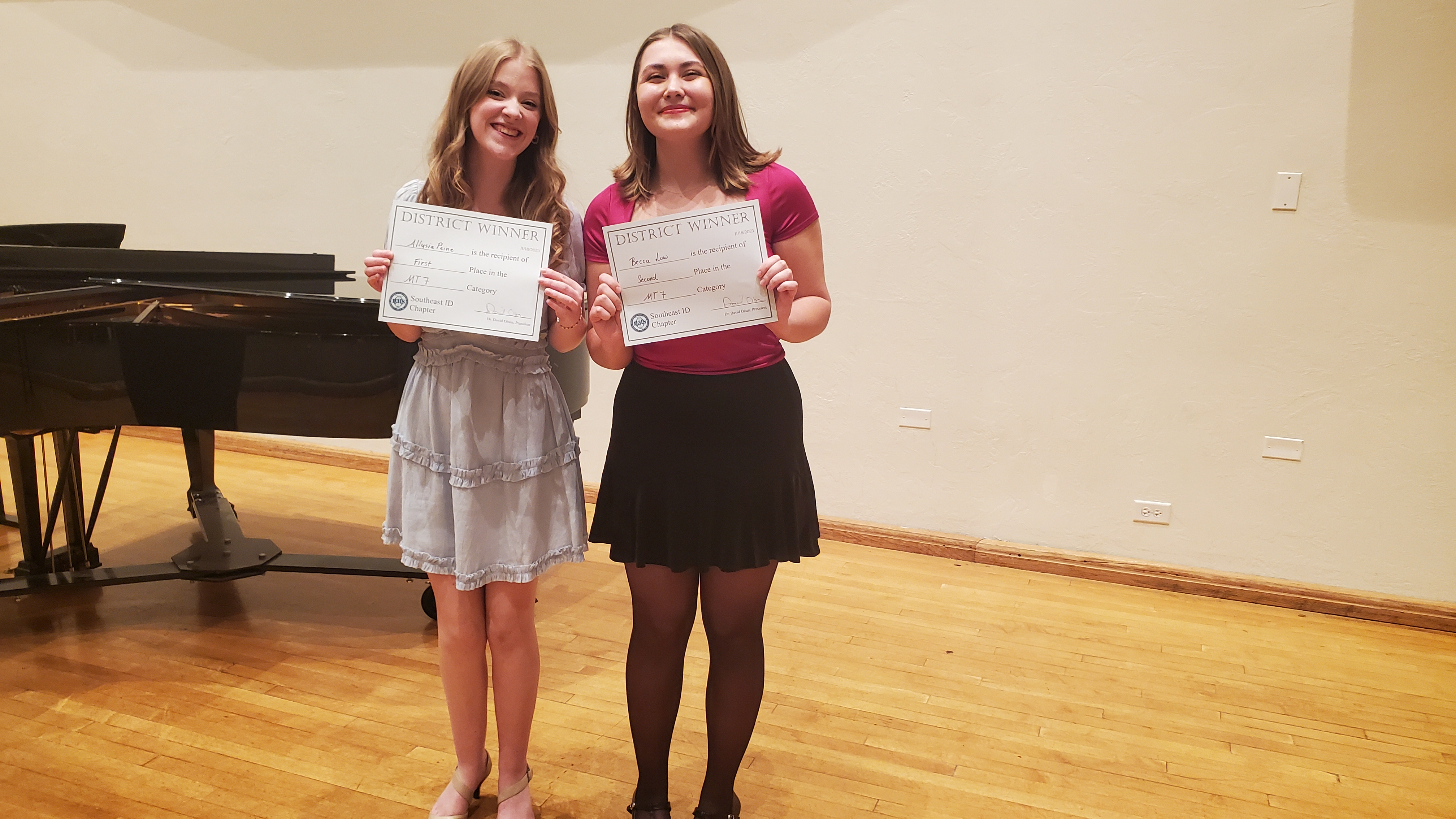 2 winning students pose with certificates in front of a grand piano