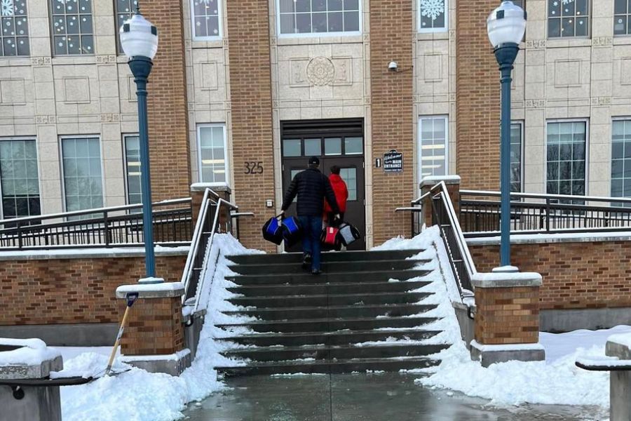volunteers deliver duffle bags of supplies to Pocatello High School. They are walking up the snow-covered front steps carrying the bags.