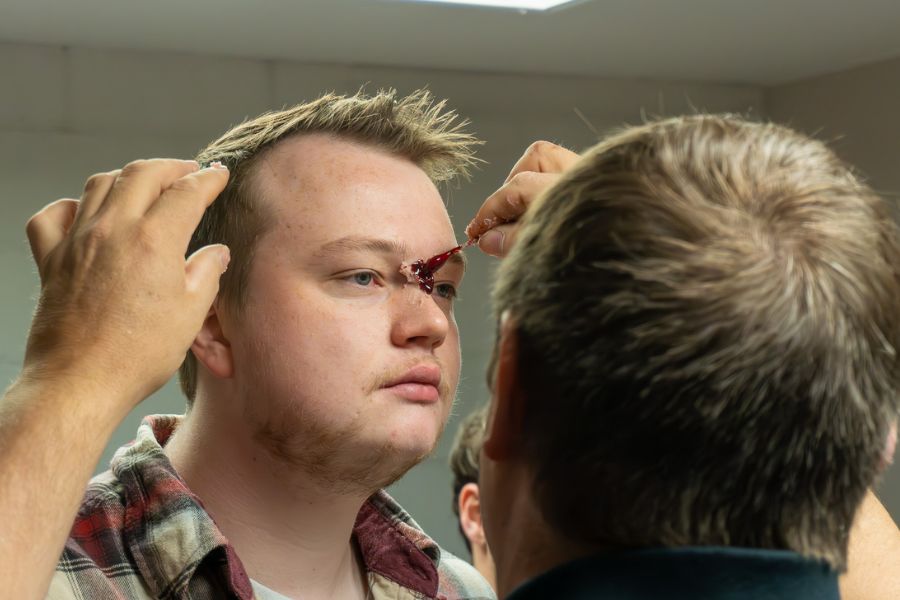 A makup artist works on a volunteer's makeup by painting an injury above their eyebrow