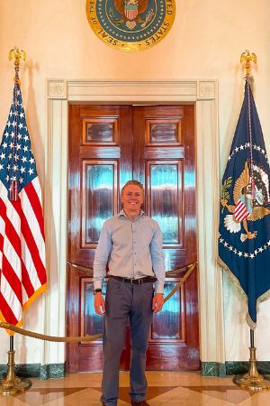 Eric Morris stands in the White House between the United States flag and another flag