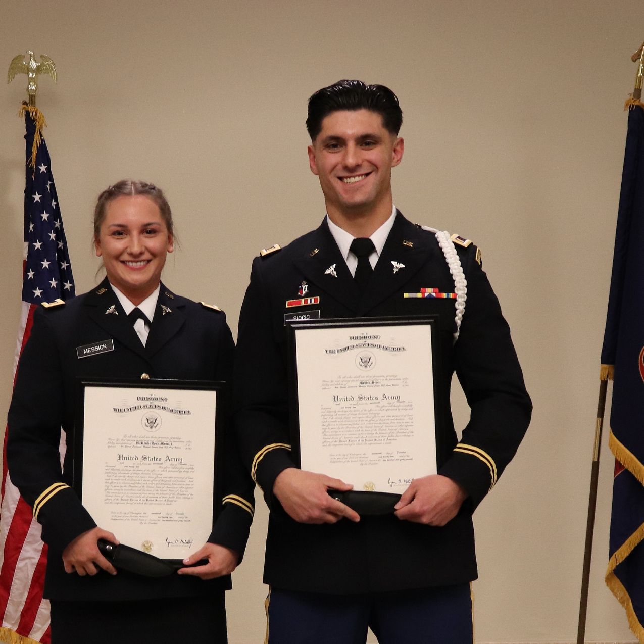 2 ROTC students dressed in their formal military uniform hold certificates and smile, in the background are the US and Idaho flags