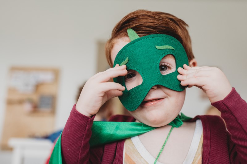 Young white boy with green mask and cape, playing superhero