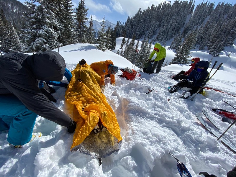 Residents training avalanche rescue, strapping practice rescue victim to back board.