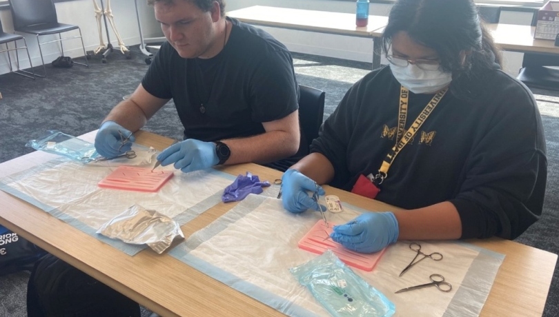 Two High school Pipeline students sitting side-by-side and learning with suturing skin substitutes at the University of Idaho through North Idaho AHEC Scrubs Camp.