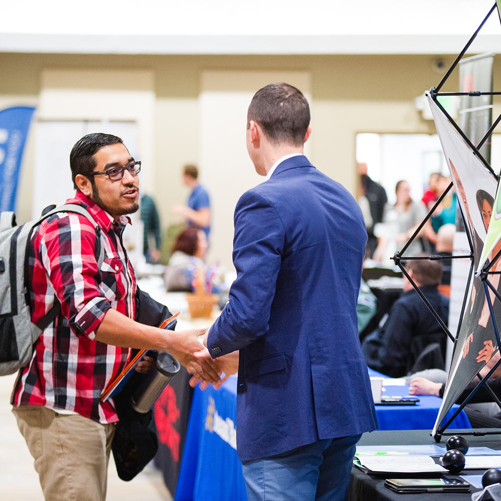 A student shaking a business professional's hand at a career fair
