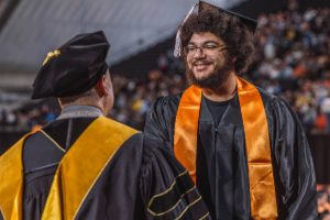 Josh Govan shake President Wagner's hand at commencement. Both are in graduation regalia.