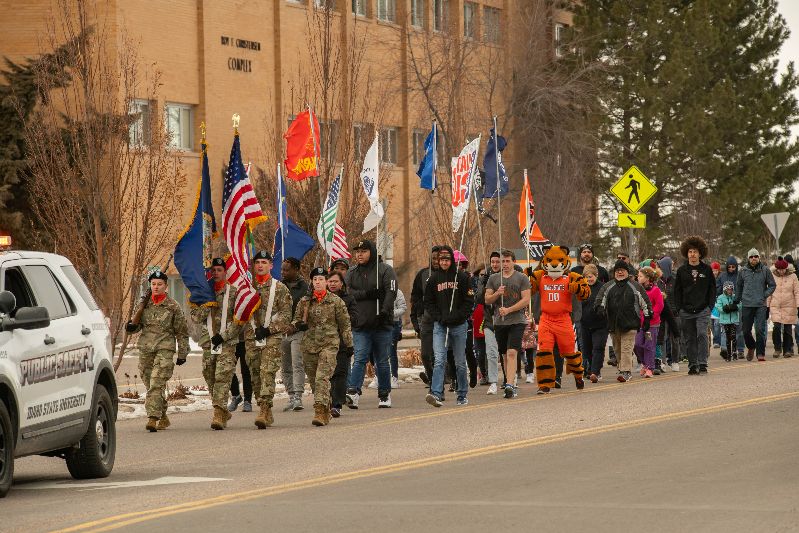 A group of people, some in military uniform, walking down a street holding flags
