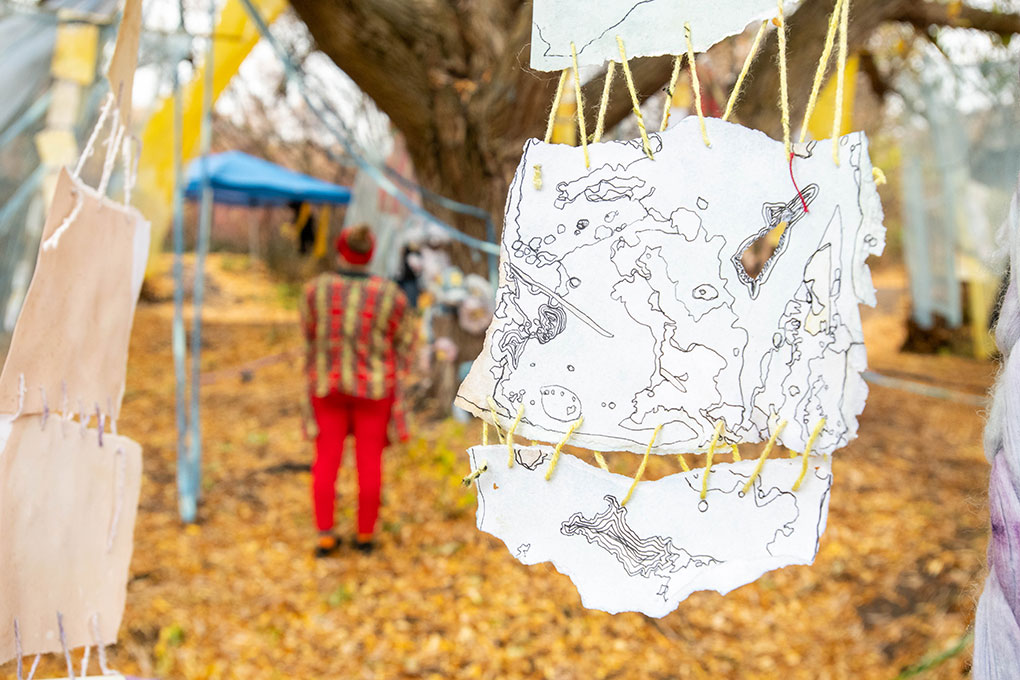 A shredded ink drawing, sewn together by yarn, is hanging in the foreground. An installation visitor is visible in the background