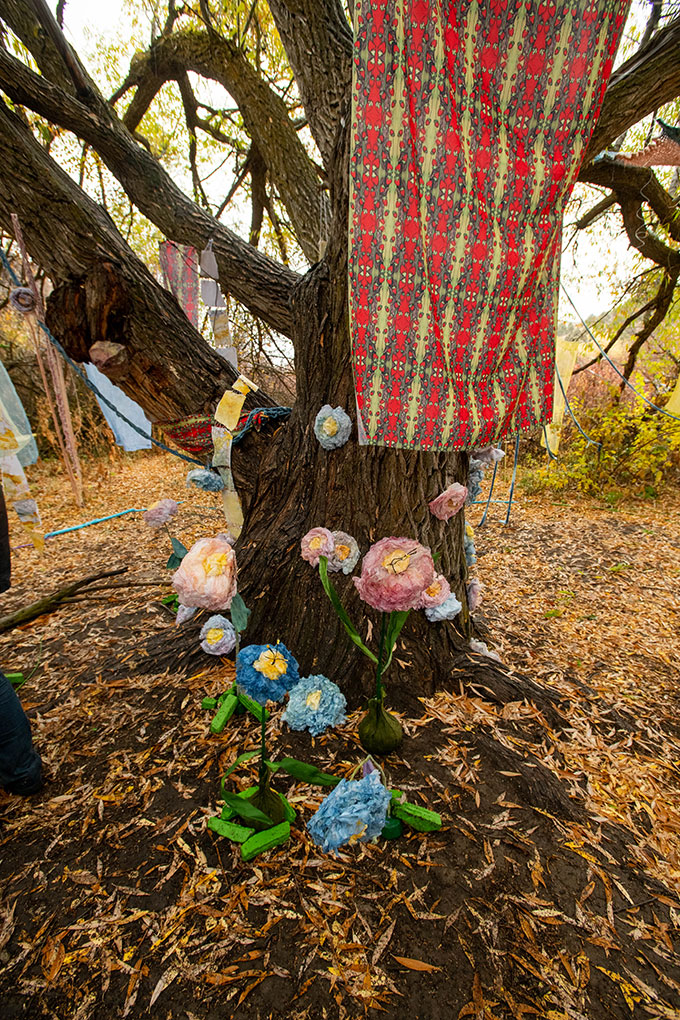 Paper flowers and colorful fabrics arranged around the trunk of a tree