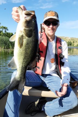 Ethan Kumm sits in a canoe on a lake holding up a fish he caught