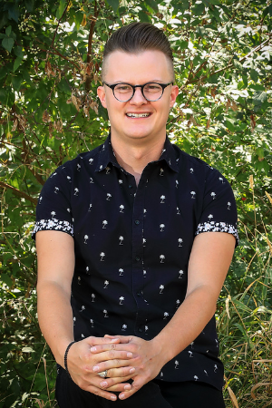 Headshot of Christopher Thomas in front of green tree leaves