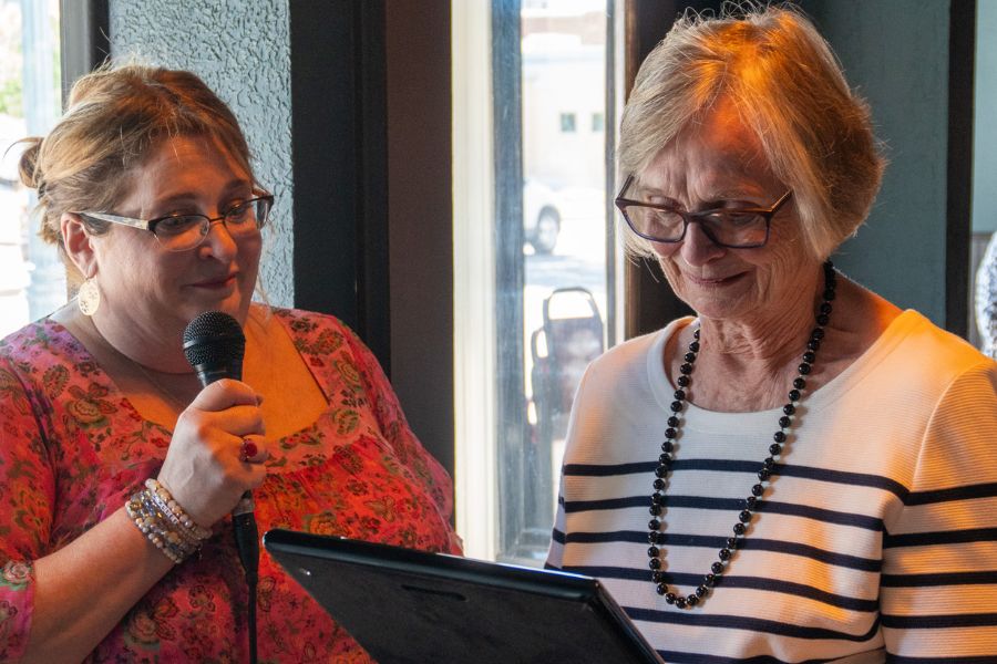 Dr. Ann Hunter is presented a plaque by her daughter, Suzanne Bentley. Ann looks fondly at the plaque, while Suzanne holds a microphone.