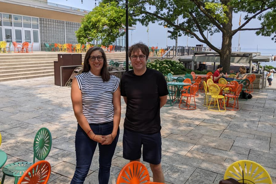 Marin and a student stand outside on a paved patio with colorful chairs and tables in the foreground and background.
