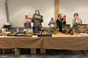 art club members stand behind a table with arts and crafts on it