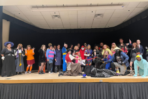 A large group of students stands together. Many of them are in Halloween costumes.