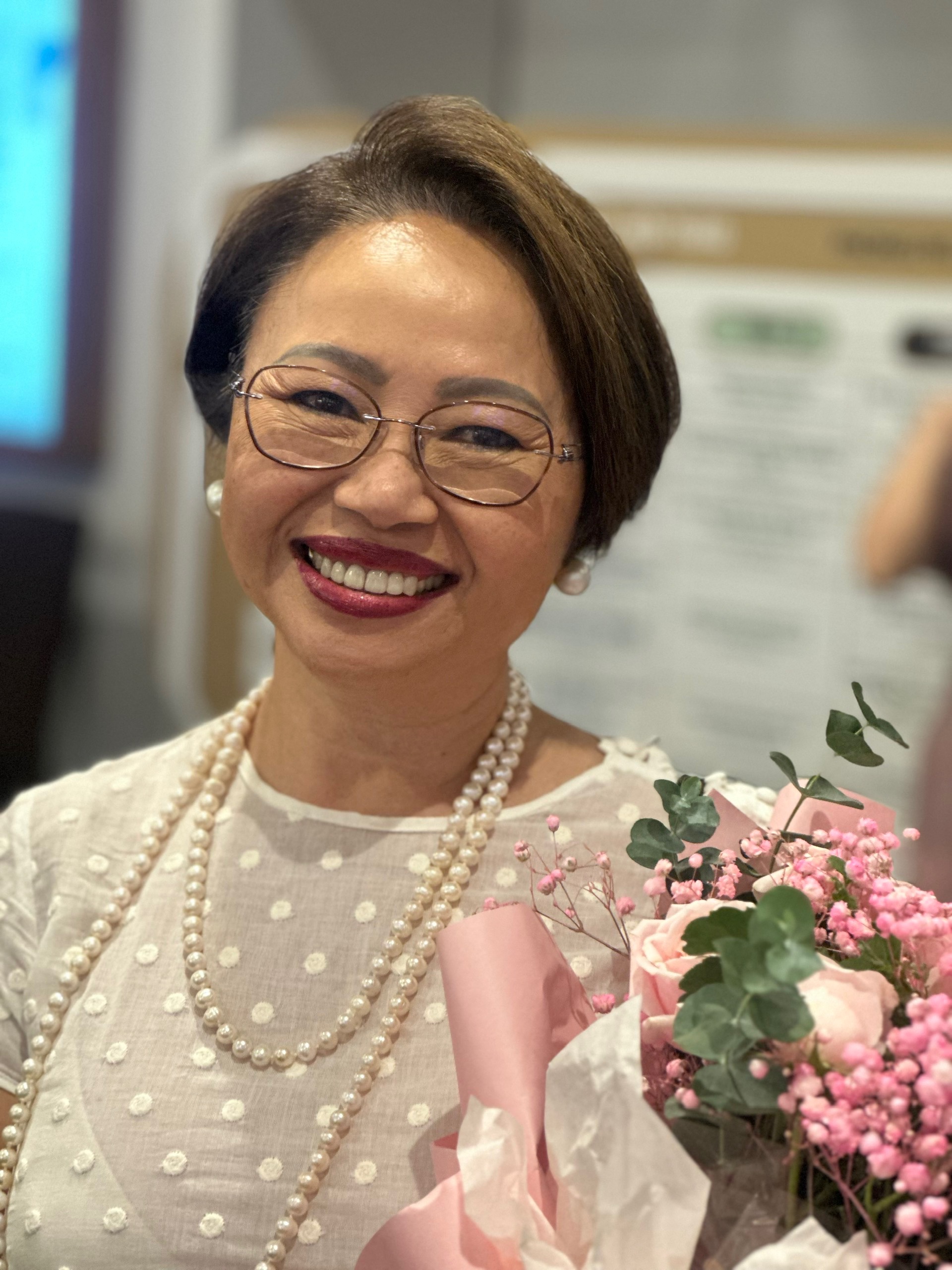 Headshot of Carina Hoang smiling. She is holding a bouquet of lilies.