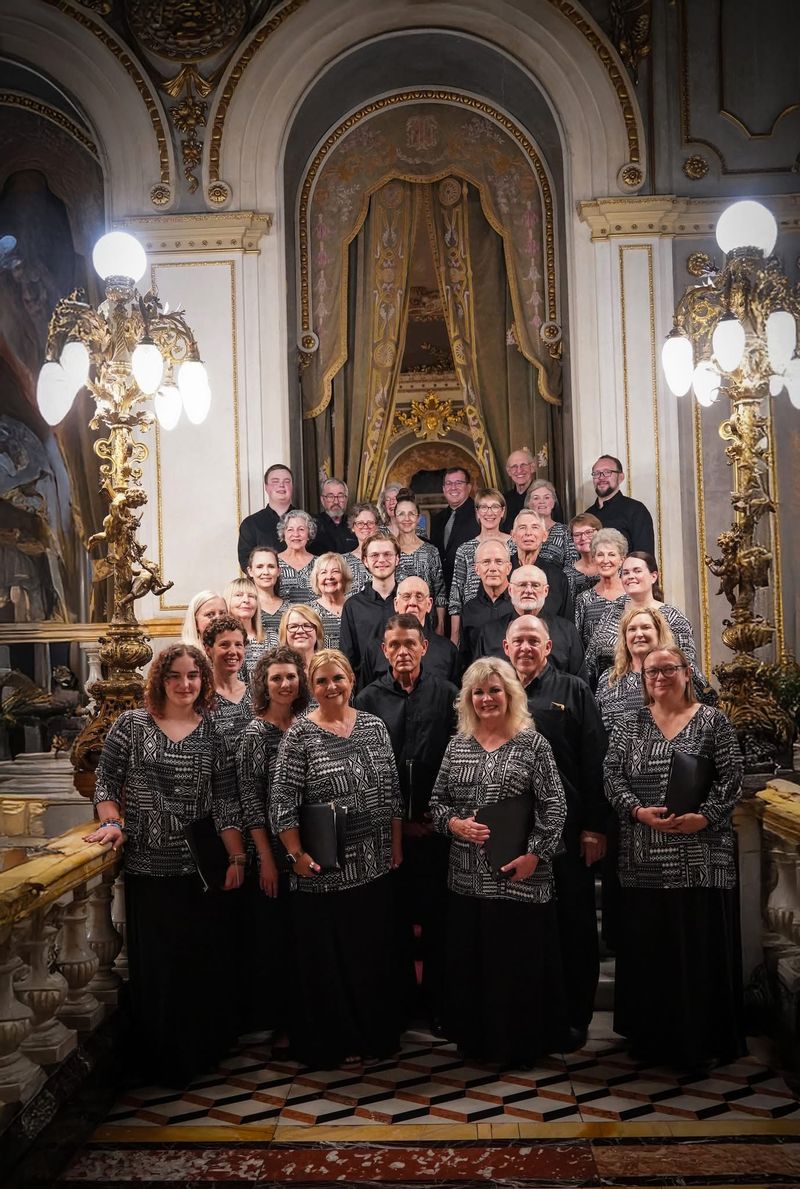 A choir group posing on a staircase in an ornate setting with decorative arches and gold embellishments.