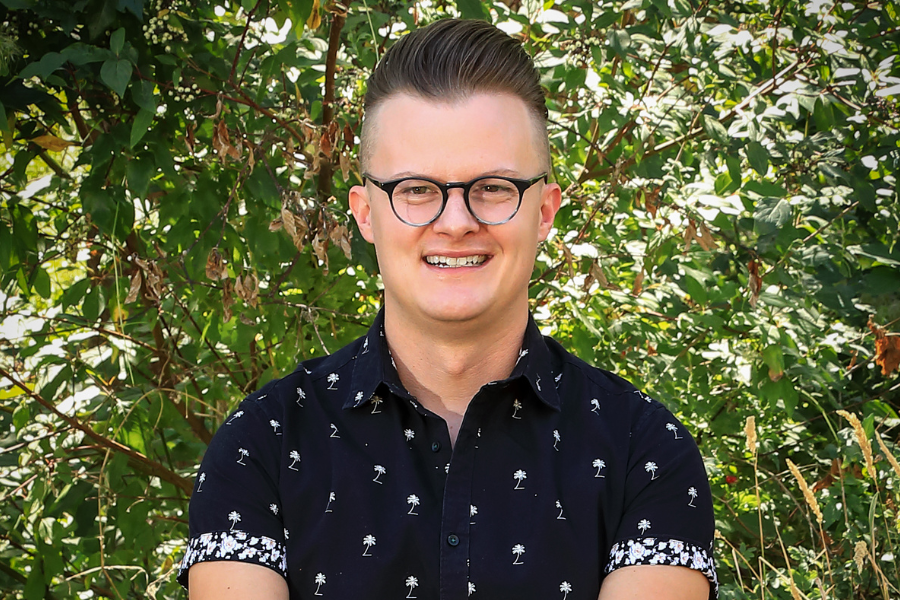 Headshot of Christopher Thomas, with a background of green tree leaves.