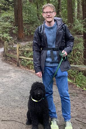 Eizzak Jordan stands outside on a hiking trail with his dog