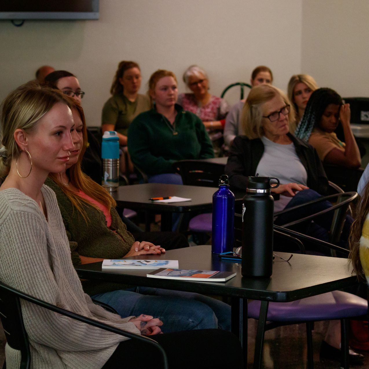 Community sits at tables facing the guest speaker at a reading event