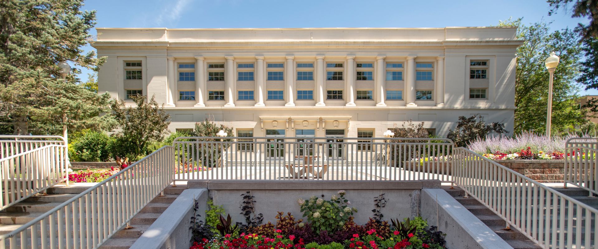 The front of Frazier Hall, a white building, with blooming red flowers in the garden bed