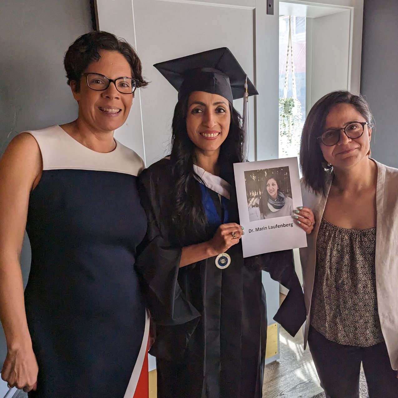 Faculty members and student Marin Laufenberg stand together posing for a photo. Marin holds a photo of herself that says 