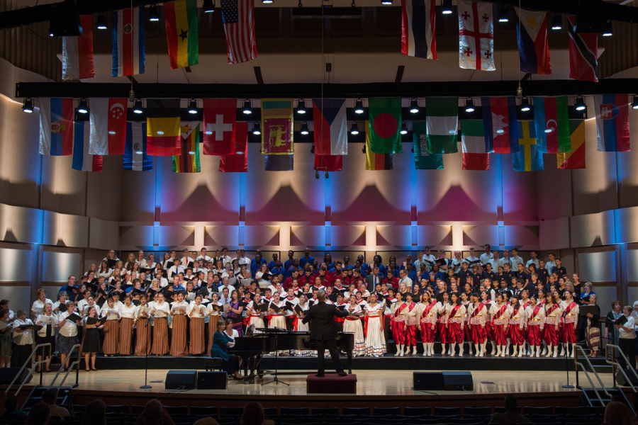 The Jensen hall in 2019 with flags above the stage and the stage is full of choirs from around the world