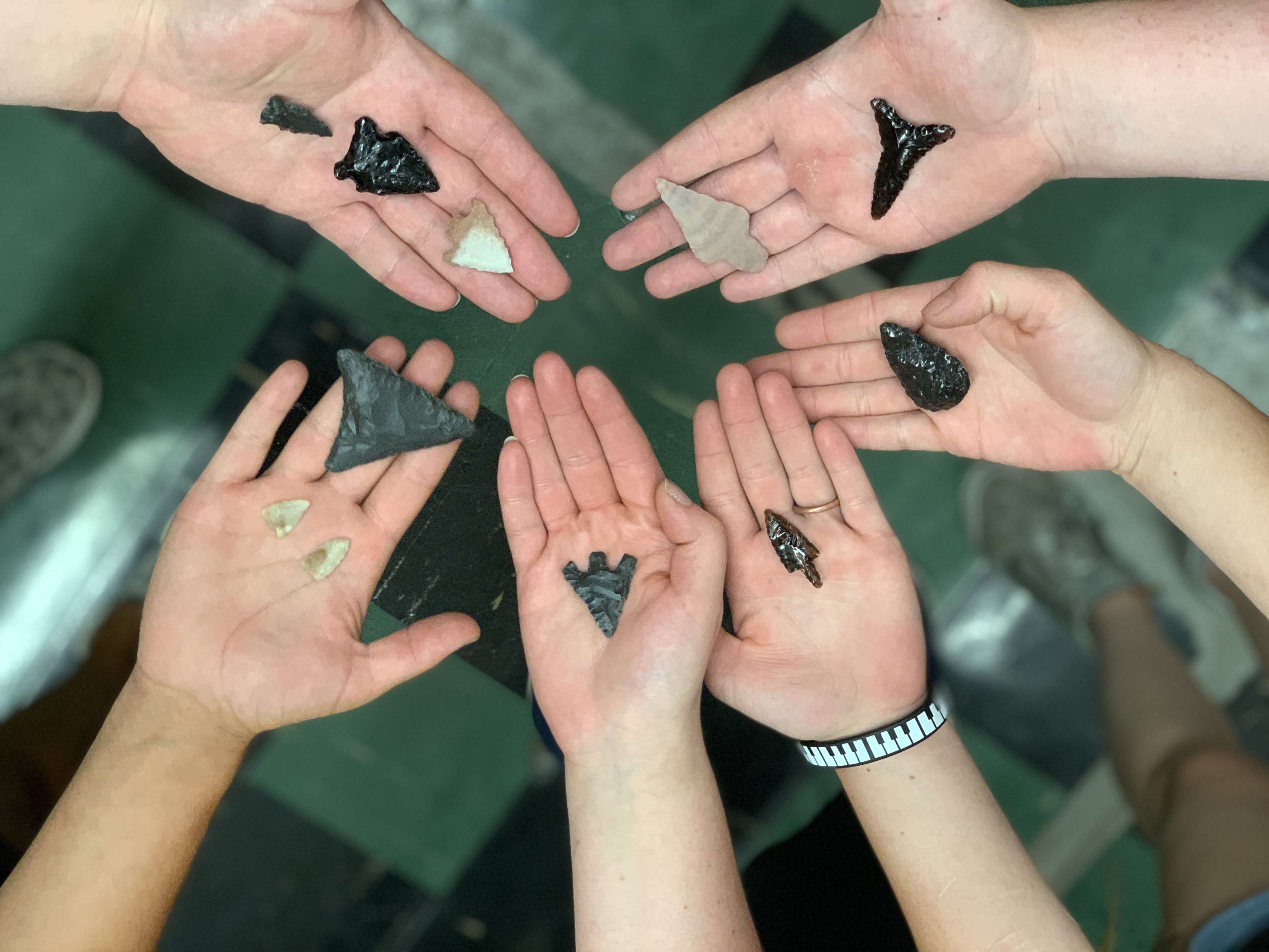 5 hands facing palm-up are holding arrowheads