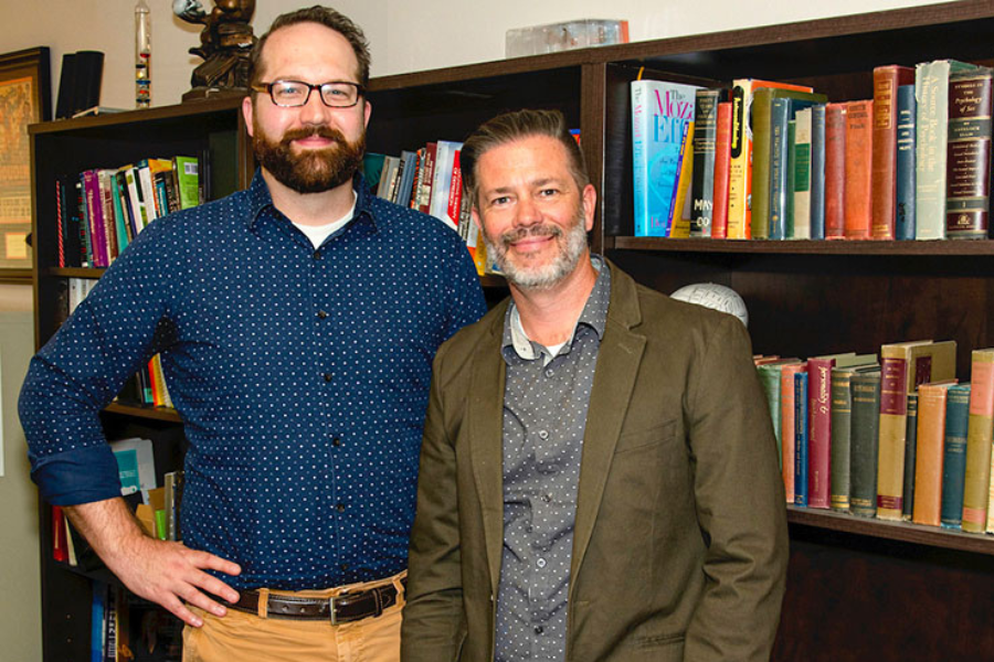 Dr. Peer and Dr. Dudgeon pose together in front of a bookshelf, smiling