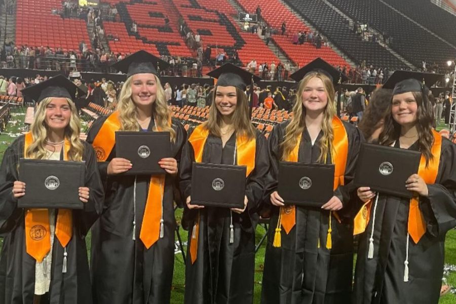 5 high school graduates in regalia hold up their diplomas