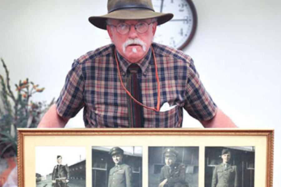 Bill McCurdy stands holding a picture frame with 4 black and white photographs. He is wearing his iconic cowboy hat.