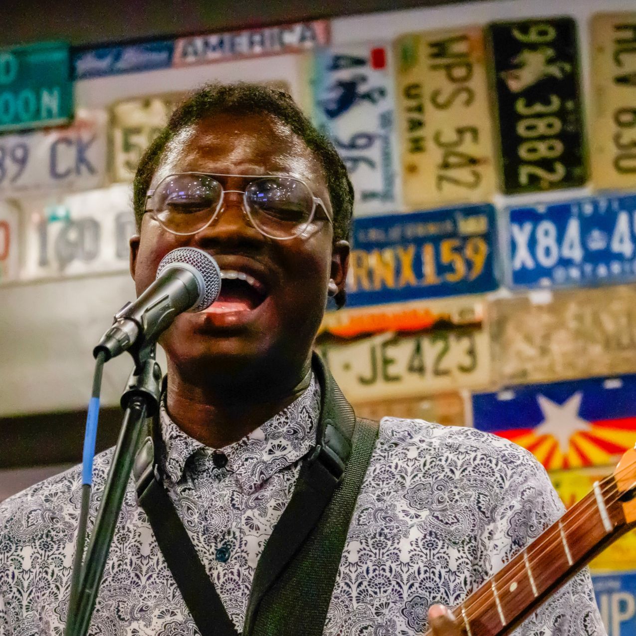 close up of ISU student singing at a microphone. He is holding a guitar.