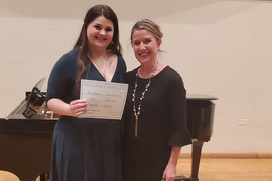 Miren Gabiola and Diana Livingston Friedley pose in front of a grand piano. Miren is holding an award certificate.