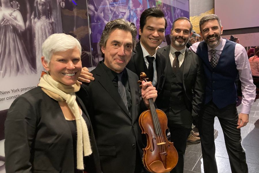 Nell Flanders stands with the four members of the Pedro Giraudo Tango Quartet. Pedro holds a violin. They are all smiling and wearing concert dress suits