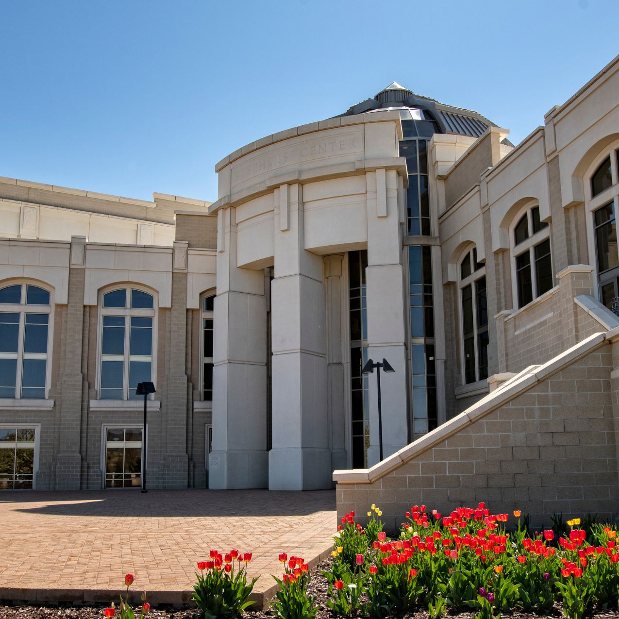 The front of the Performing Arts Center in the daytime. The building is a tall, columnar white stone with long windows. The sky is blue.