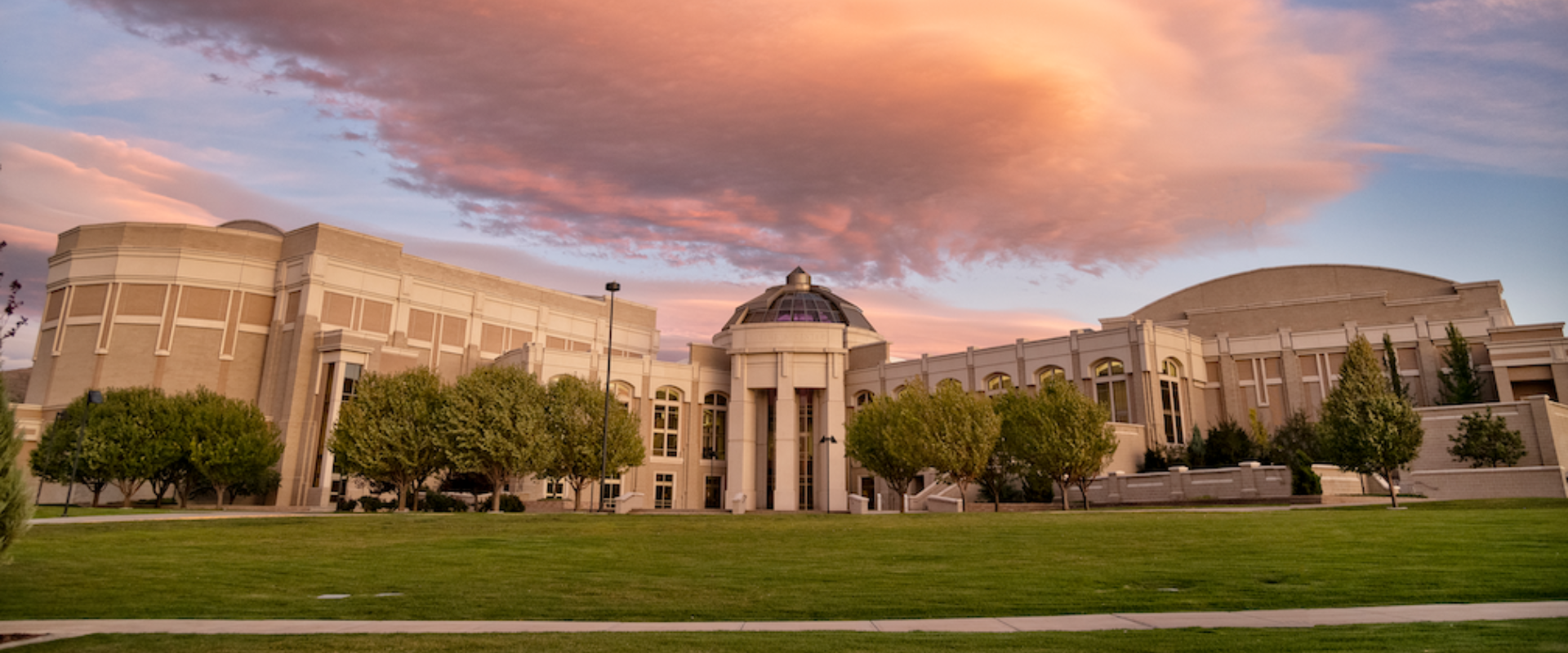 The front of the Stephen's Performing Arts Center lit up by the sunset with a large purple and pink cloud overhead