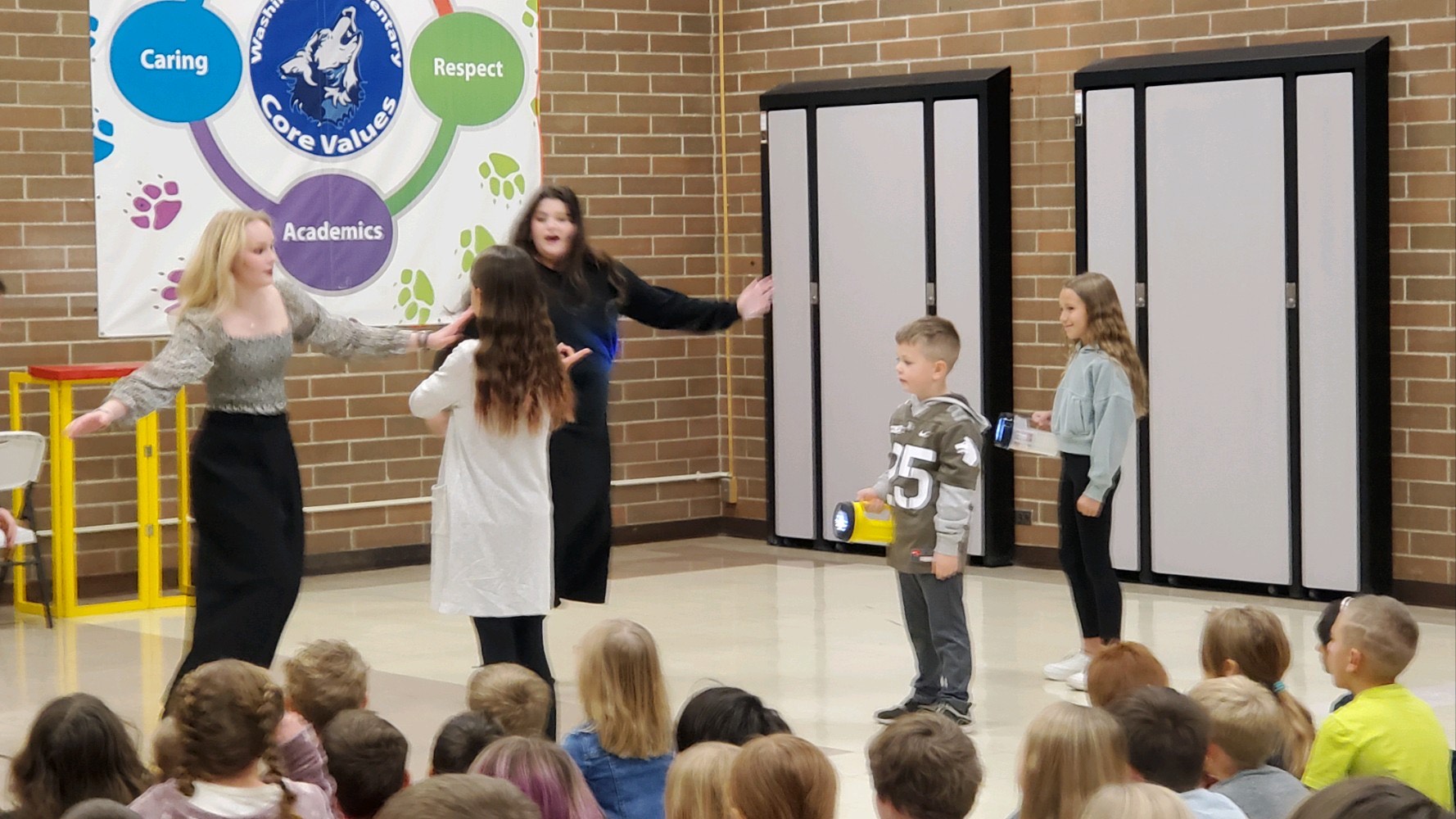 2 ISU students perform opera while one elementary student conducts with a music baton, and two shine lights on them