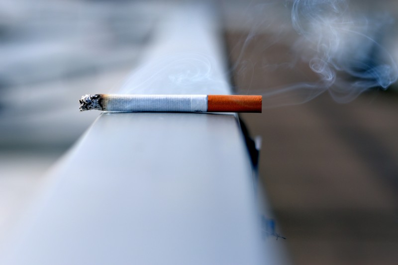 A smoking cigarette sits on a ledge.