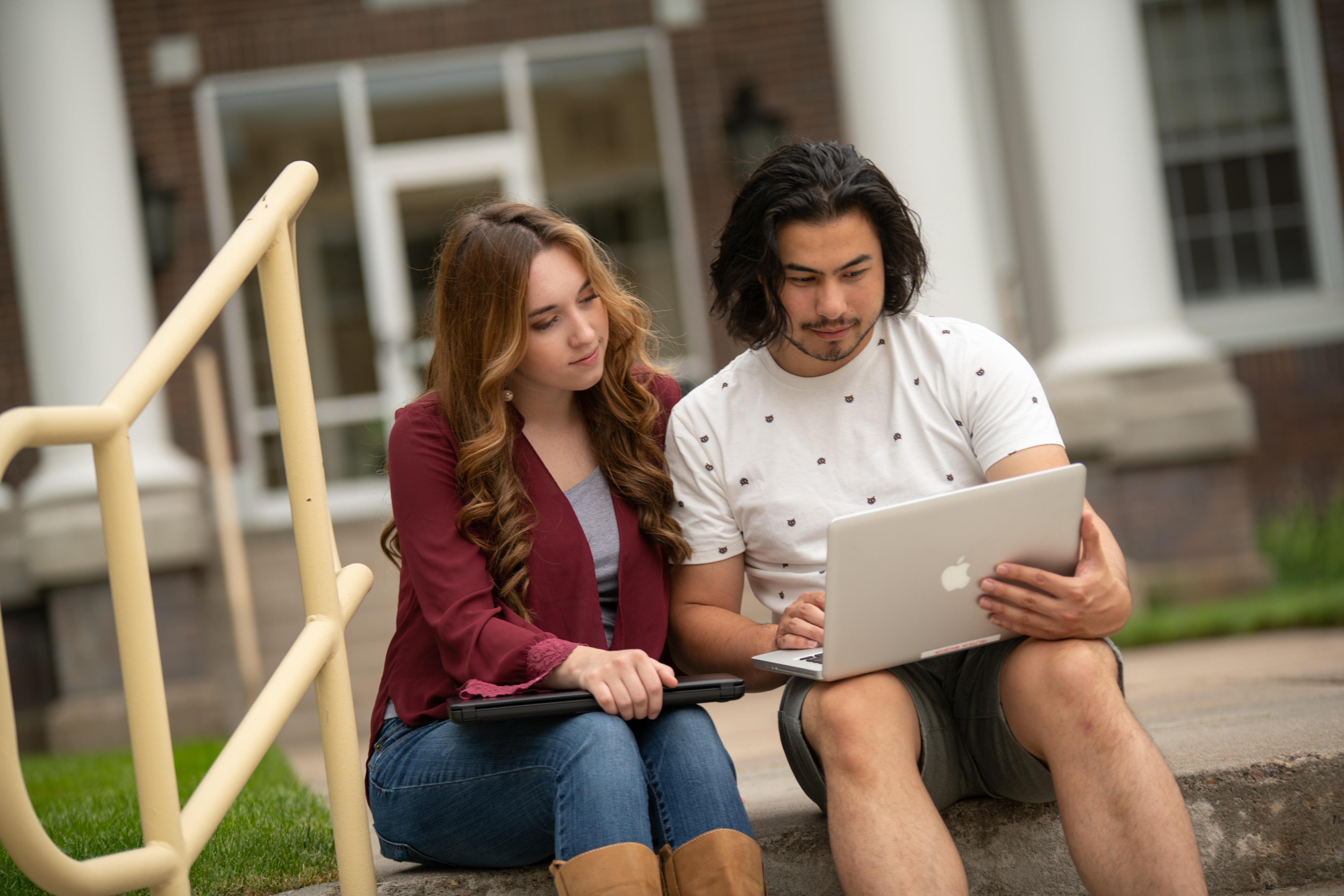 Two students seated outdoors looking at a laptop