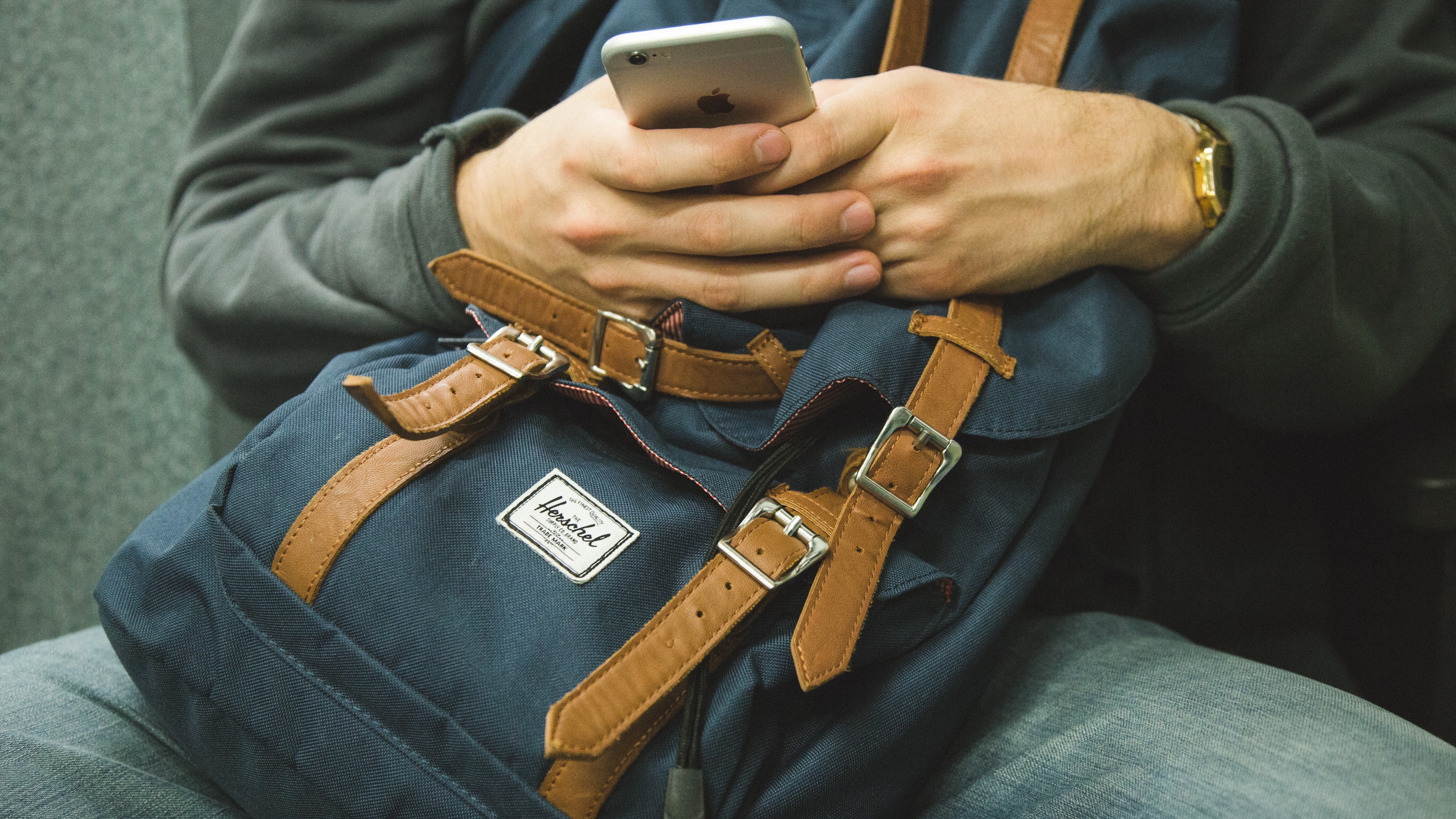 Student sitting with a backpack on their lap and using their phone