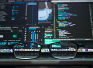 A computer showing website coding and a pair of eyeglasses