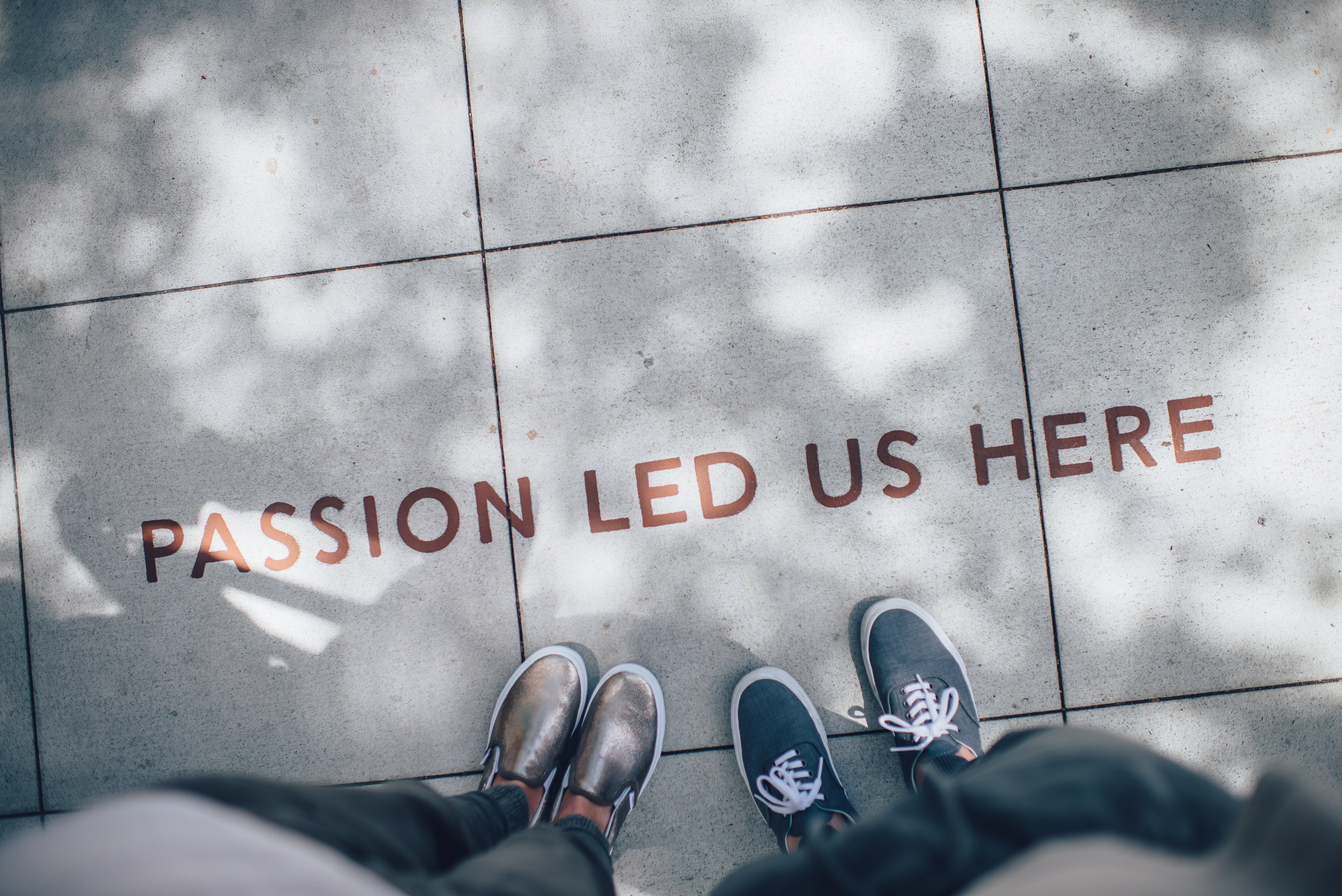 Two people standing on concrete with lettering. Text: Passion lead us here