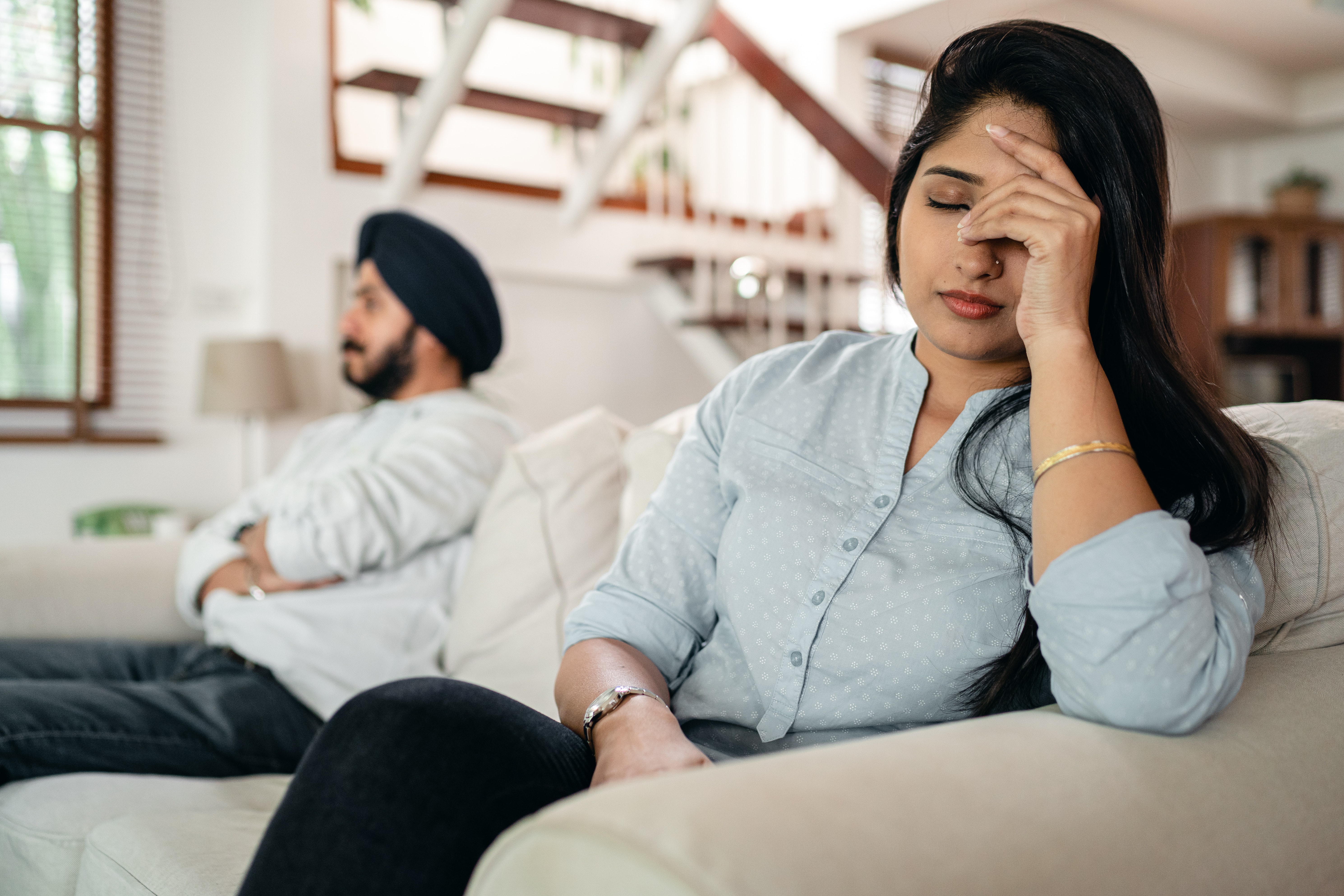 Two people sitting on a couch with one facepalming while the other looks away