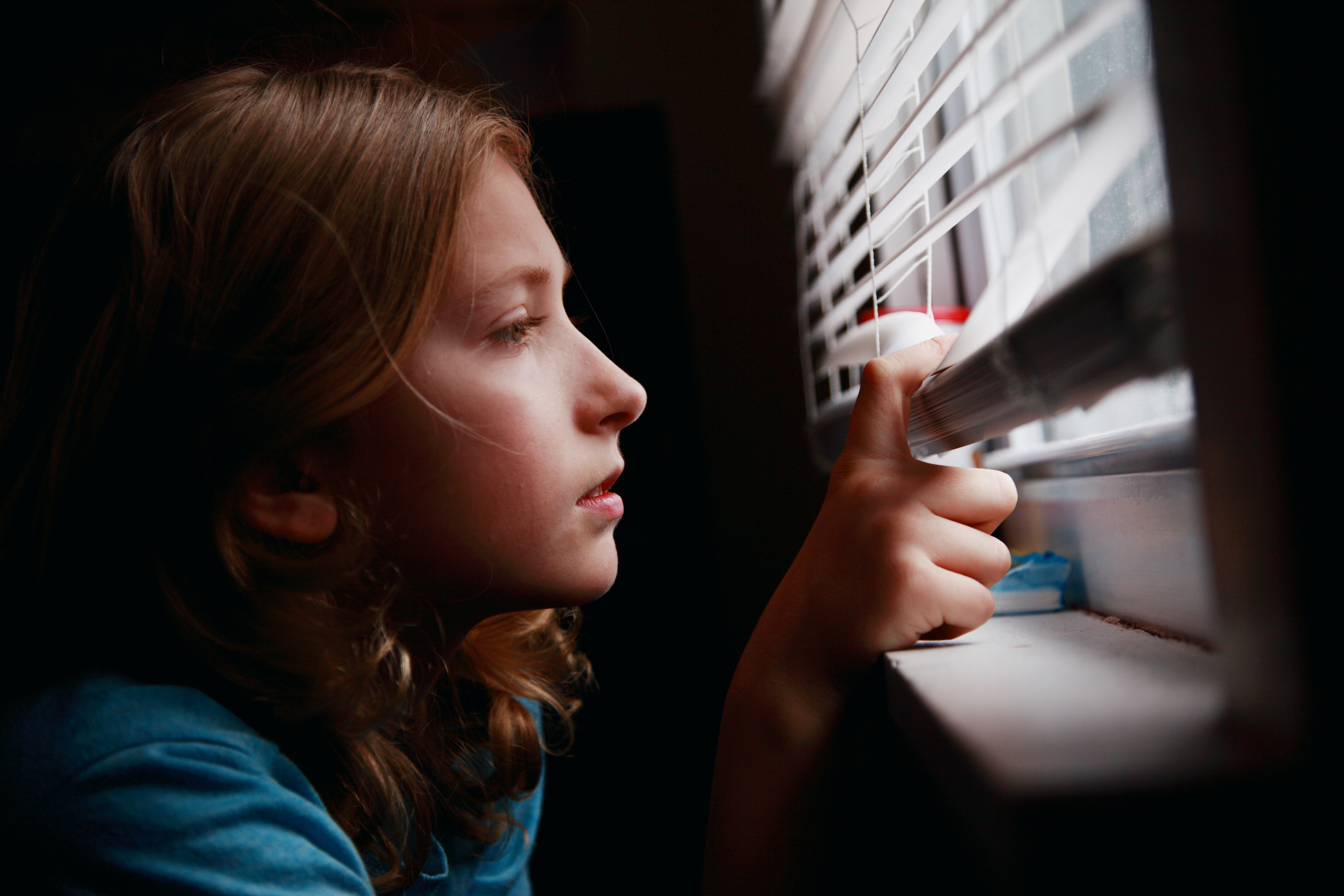 A person peering through her window blinds