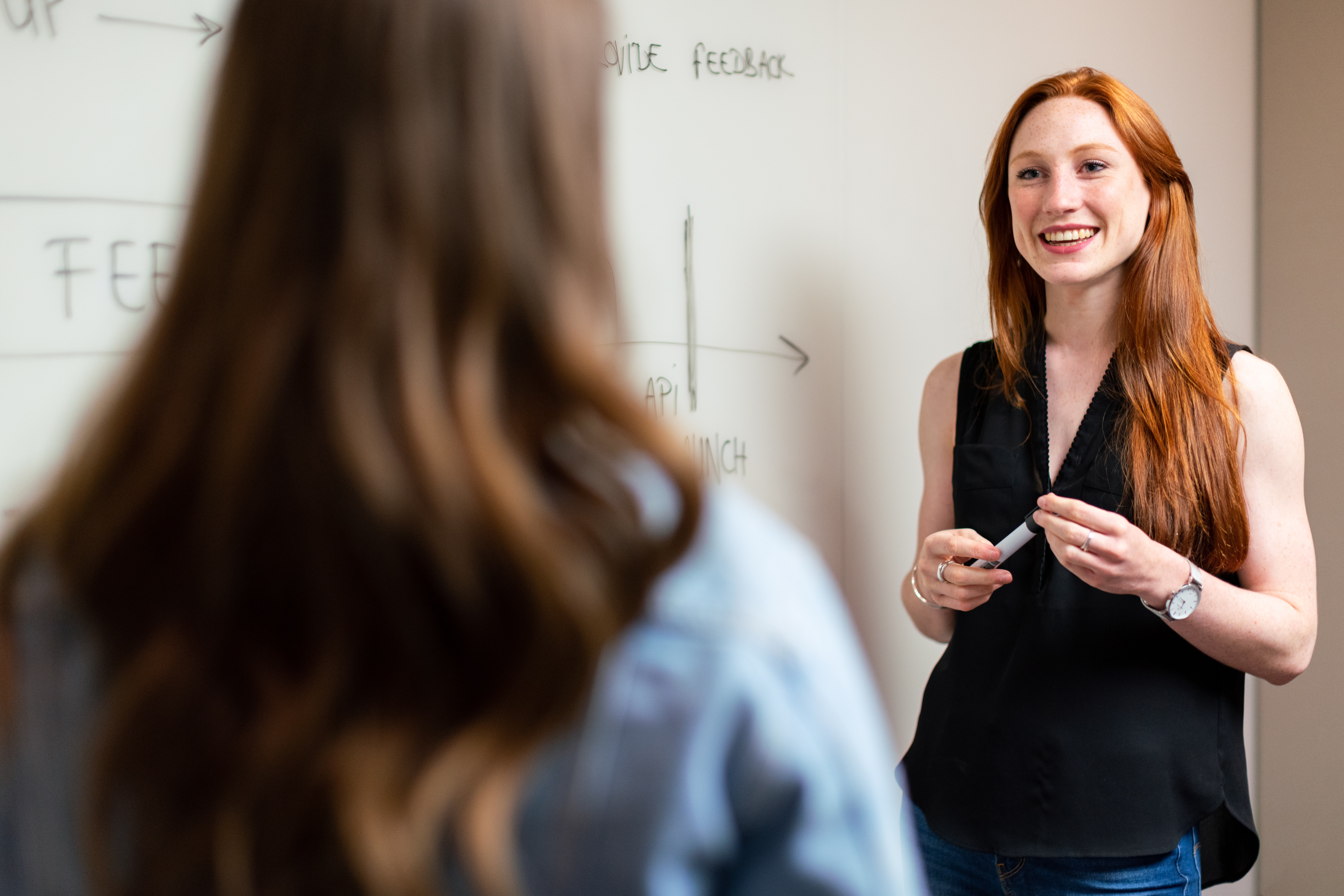 Two people talking next to a white board