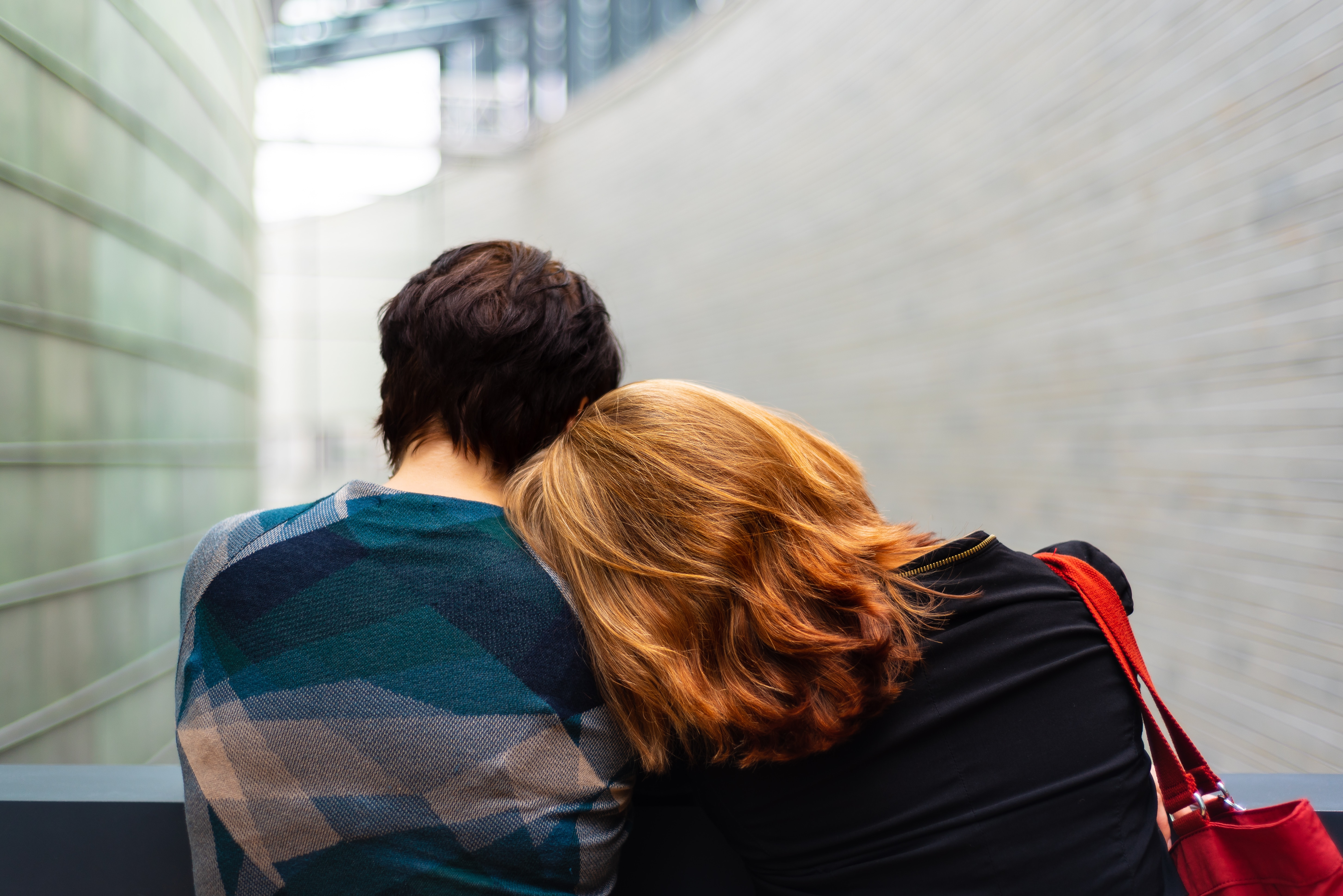 A couple sitting at a bench leaning their heads against each other