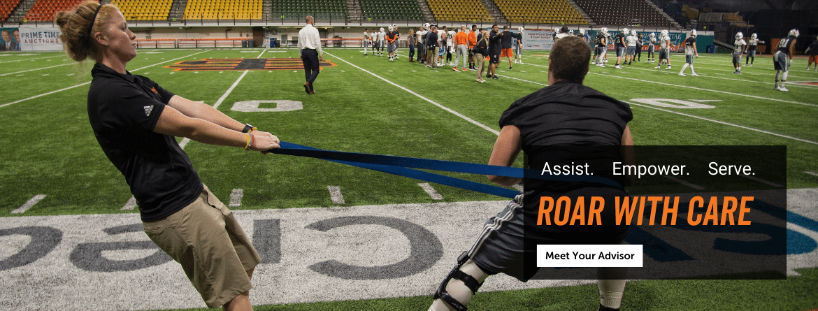 Top text reads: Assist. Empower. Serve. Center Text Reads: Roar with Care Bottom text Reads: Meet you advisor (link button) Image description: An athletic trainer helping an athlete stretch. Football practice in the background.