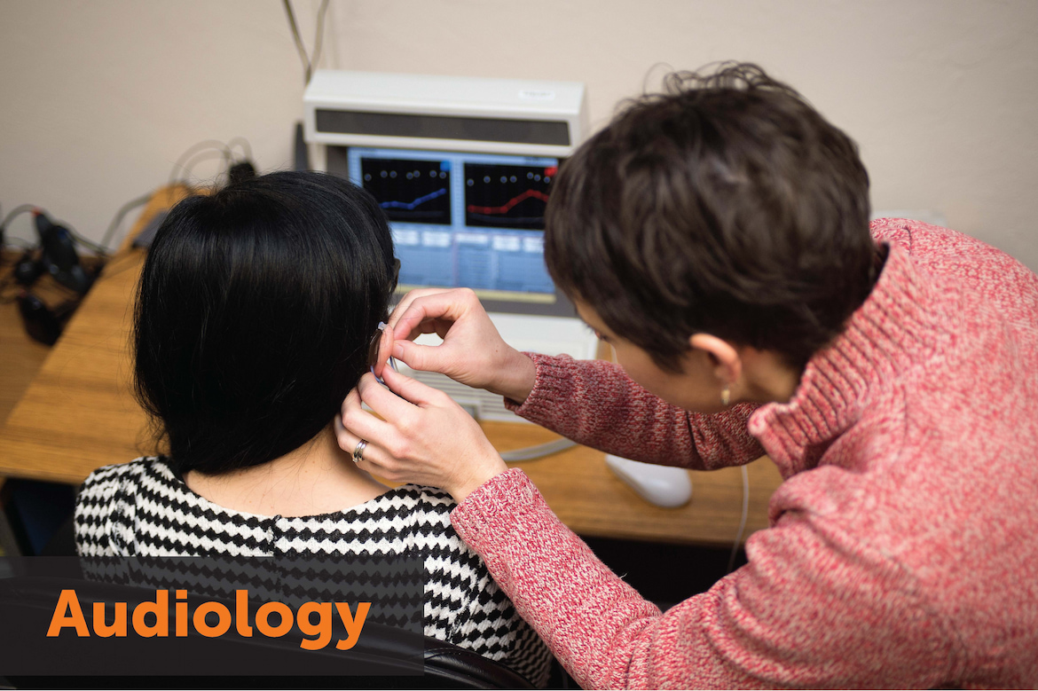Image: A woman fitting a person with a hearing aid. Text: Audiology. Links to Audiology Home Page.